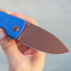 SHOOZIZ HAN306-LMRG folding knife held in hand, rose gold PVD 14C28N steel blade, blue Micarta handle.