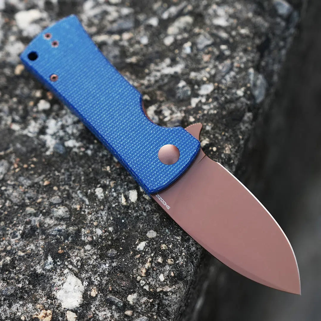 SHOOZIZ HAN306-LMRG folding knife open on stone, 14C28N steel blade with rose gold PVD finish, blue Micarta handle.