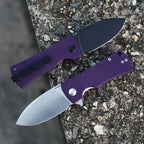 SHOOZIZ HAN306-PGS and PGB purple G10 folding knives open on stone, displaying satin and black PVD blades.