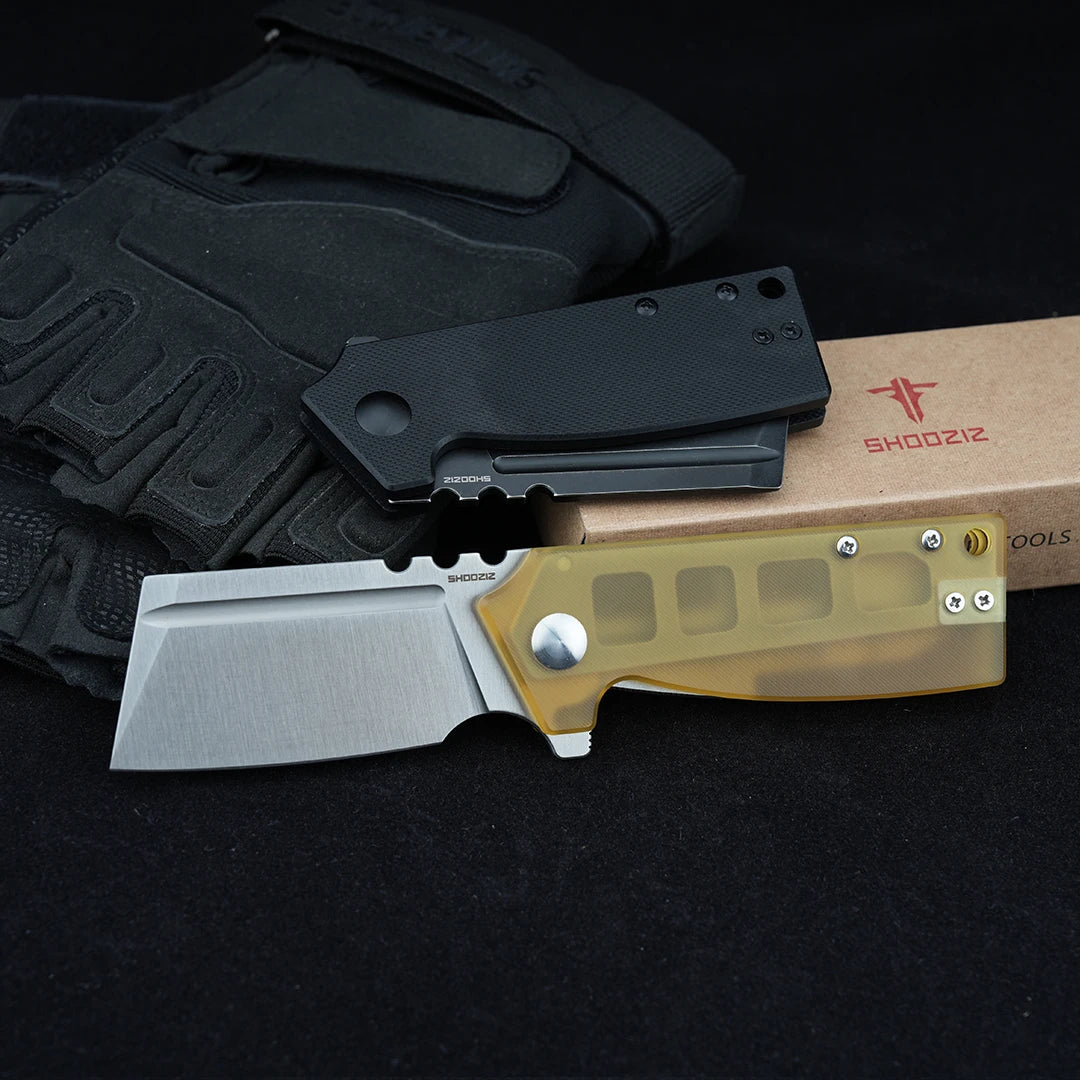SHOOZIZ HAN307-BGB and HAN307-JUS folding knives displayed with tactical gloves and a box, black G10 and Ultem handles, black background.