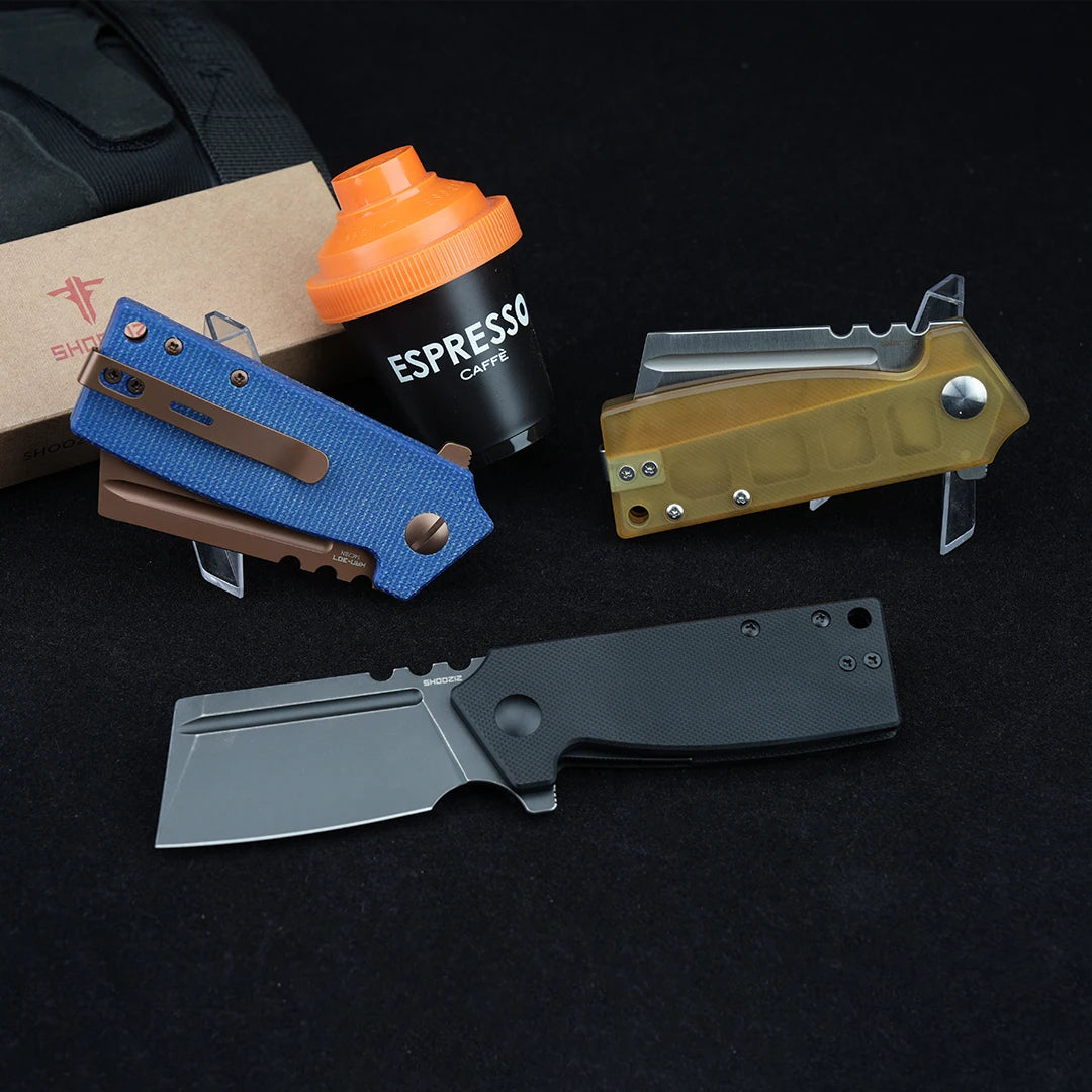 SHOOZIZ HAN307-LMRG, BGB, and JUS folding knives in an EDC scene, featuring blue Micarta, black G10, and Ultem handles with a coffee cup and box.