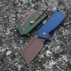 SHOOZIZ HAN307-LMRG and HAN307-GMRG folding knives closed on textured cobblestone, blue and green Micarta handles with rose gold PVD blades.