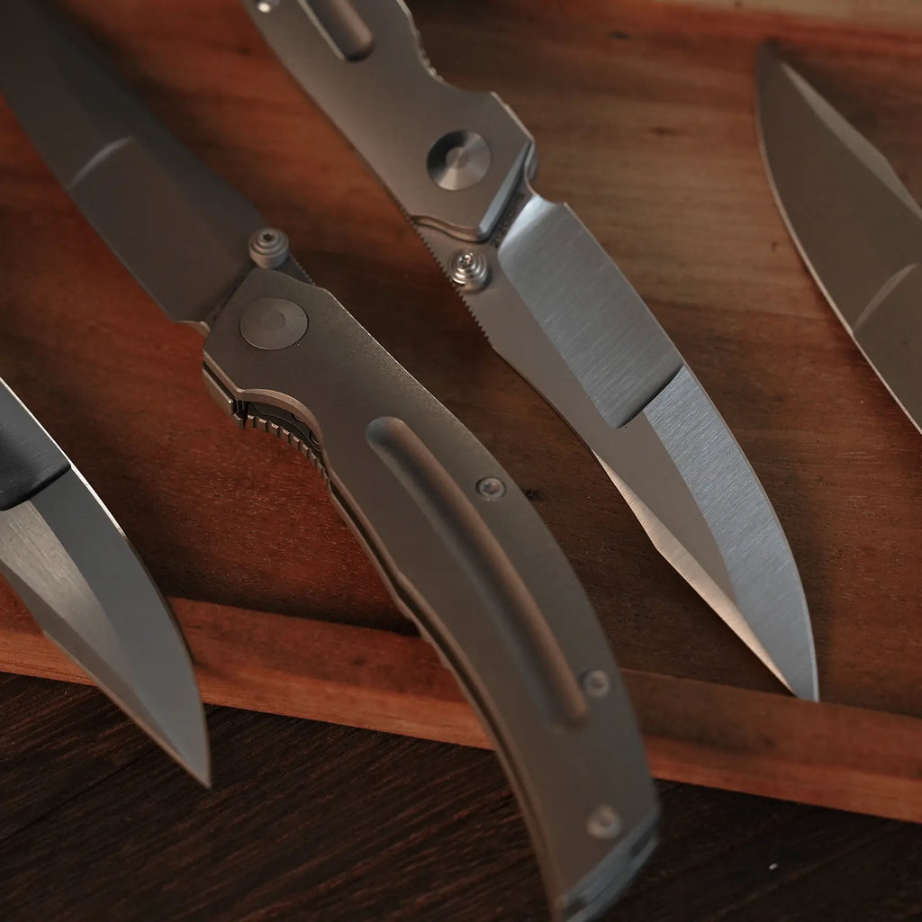 SHOOZIZ SERPENT series folding knives on wooden board, featuring TC4 titanium frame lock, satin and black stonewashed ELMAX steel blades.