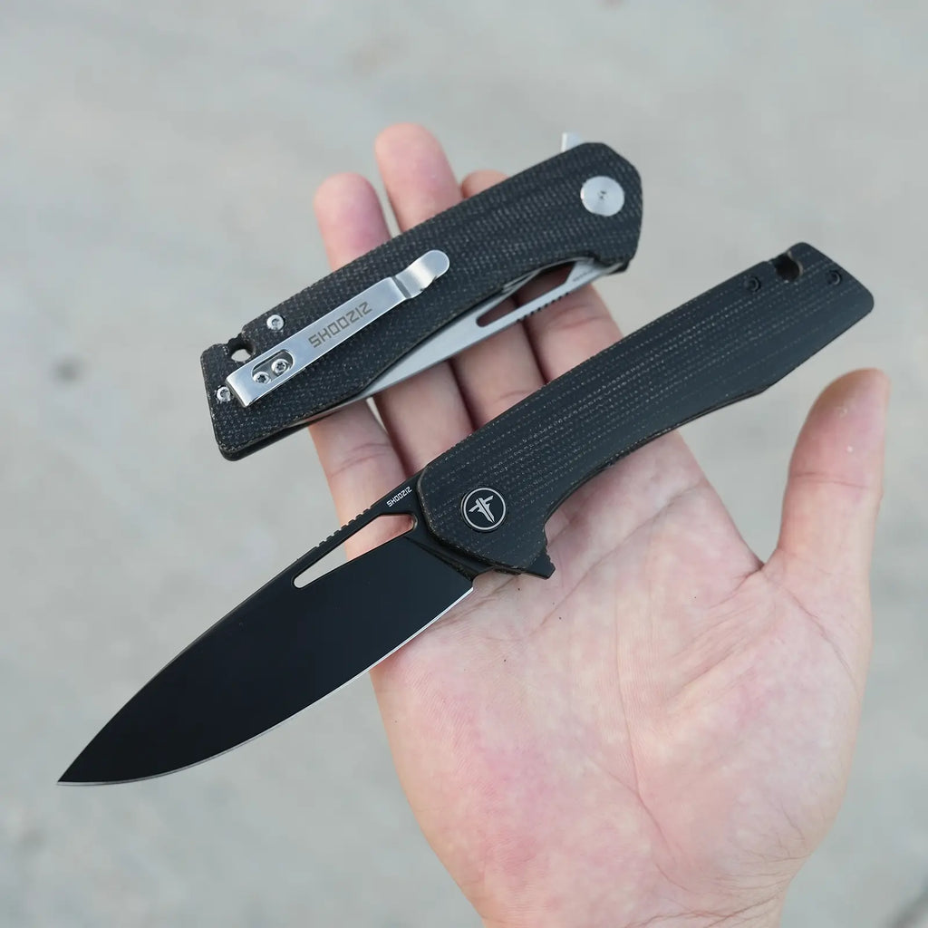 SHOOZIZ XUN120-BMB folding knife open in hand, black PVD D2 steel, black Micarta handle, alongside a folded XUN120-BMS satin blade model.