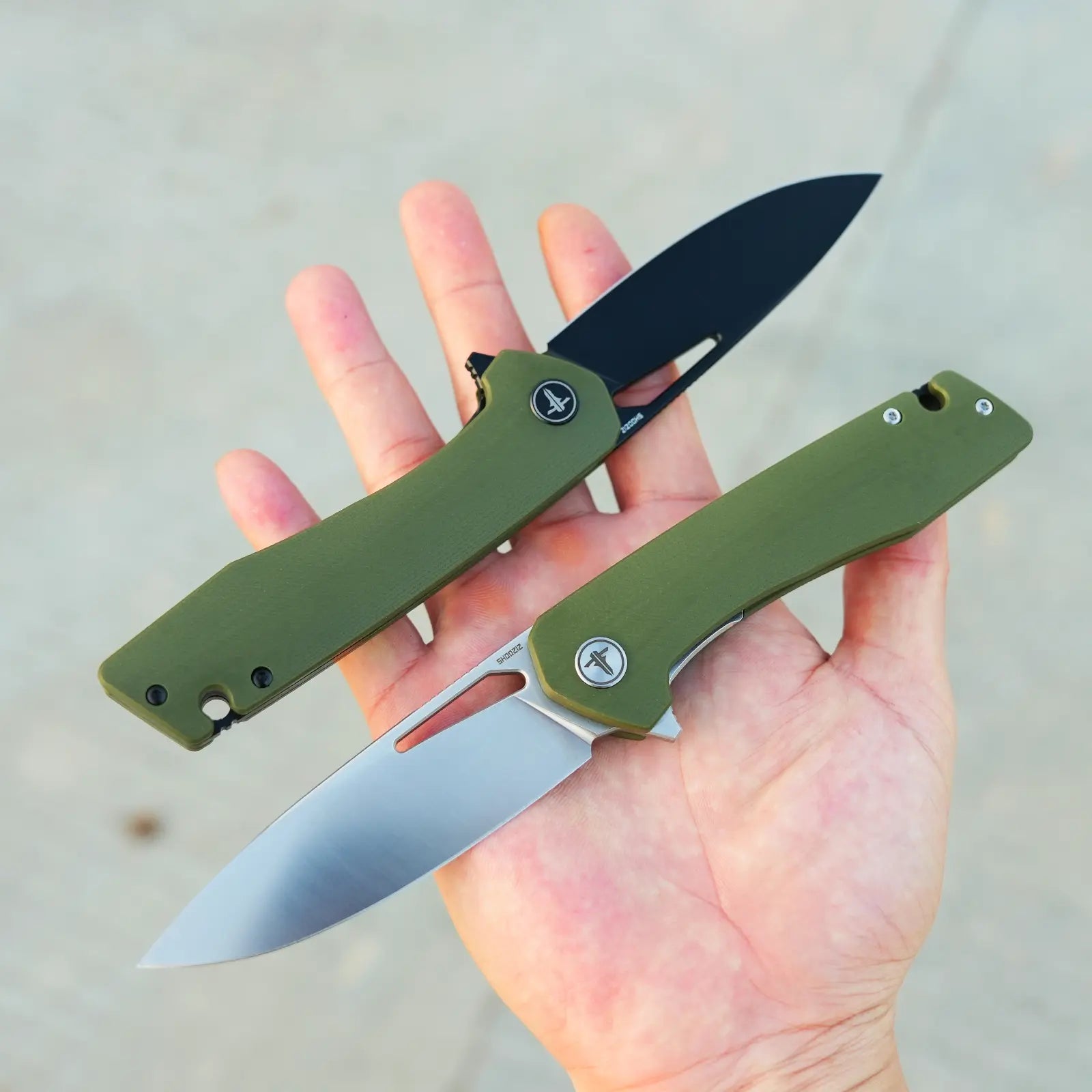 SHOOZIZ XUN120-GGS and XUN120-GGB green G10 folding knives open in hand, showing the satin D2 blade and black PVD blade variations.