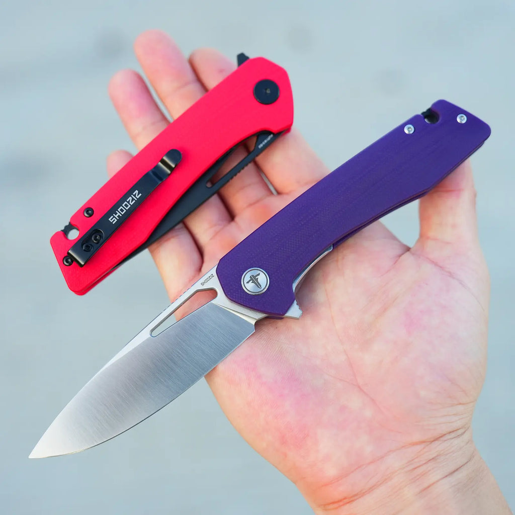 SHOOZIZ XUN120-PGS purple G10 satin blade folding knife open in hand, next to a folded XUN120-RGB red G10 black PVD model.