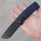 SHOOZIZ XUN122-BGB black PVD folding knife held in hand close-up, black G10 handle, black steel bolster.